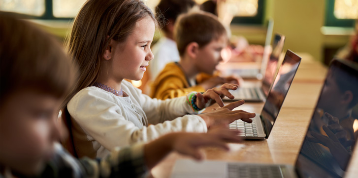 Group of elementary students using computer on a class at school. Focus is on smiling girl.