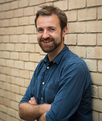 Kit Yates with his arms crossed, leaning against a wall