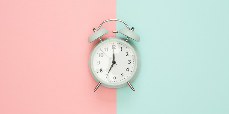 An old fashioned alarm clock on a half pink half blue background